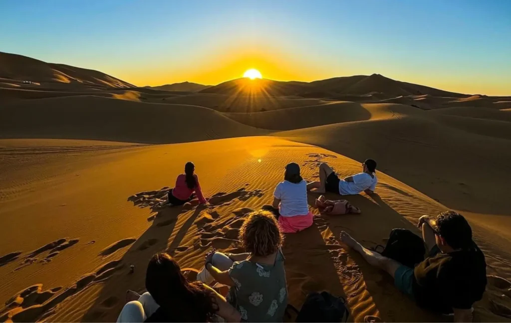 A group of travelers watching a golden sunset over the Erg Chebbi sand dunes in the Sahara Desert, a highlight of a Morocco itinerary 6 days.