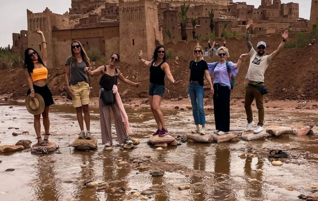 A group of happy travelers crossing the river at Ait Ben Haddou during their Morocco itinerary 6 days.