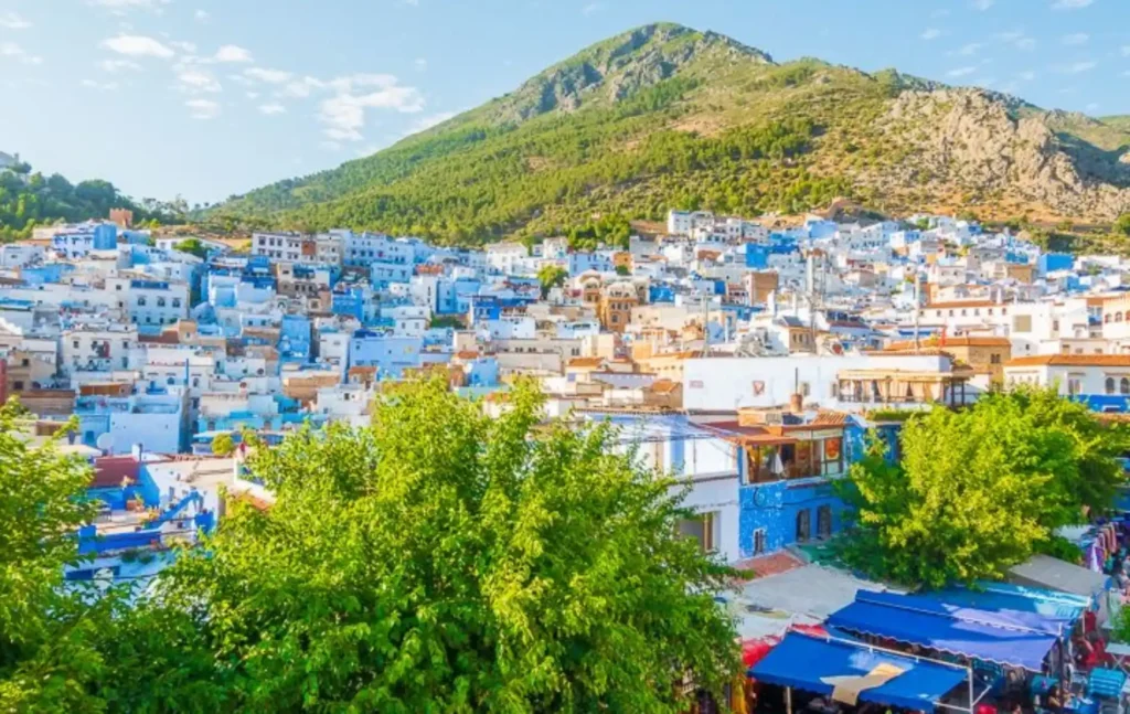 Morocco itineraries showcasing the blue-painted houses of Chefchaouen nestled at the foot of the Rif Mountains under a cloudy sky.