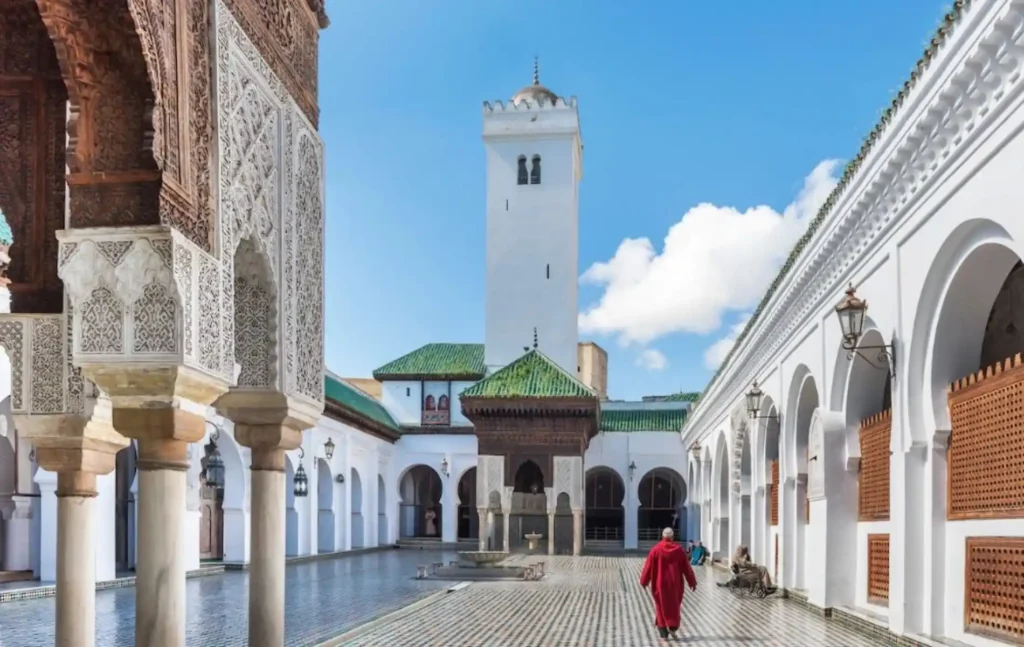 The intricate mosaic courtyard and white minaret of the Al-Quaraouiyine Mosque in Fes, Morocco.