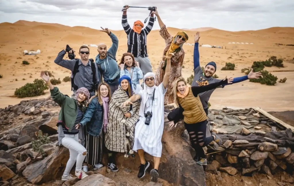 A group of happy tourists posing on a desert ridge with golden dunes in the background during their 10 days Morocco itinerary.