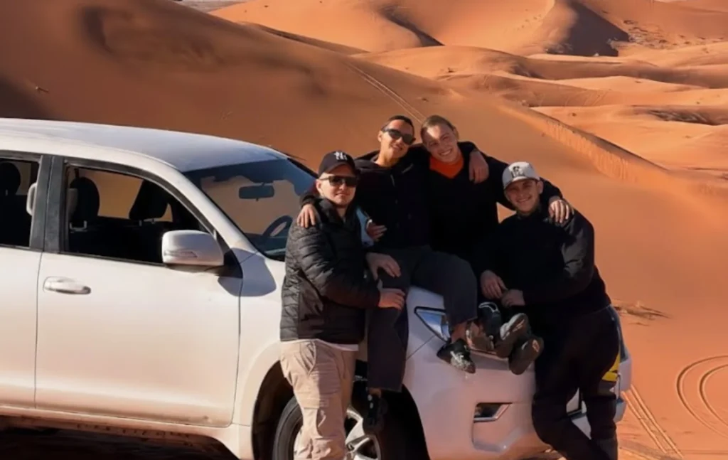 Our group with a white 4x4 SUV on the sand dunes during their 12 days in Morocco desert expedition.