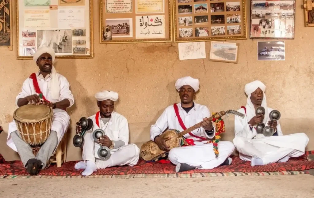 Four musicians in traditional white robes playing instruments during a Gnawa music performance, often enjoyed by travelers on a Merzouga jeep tour.