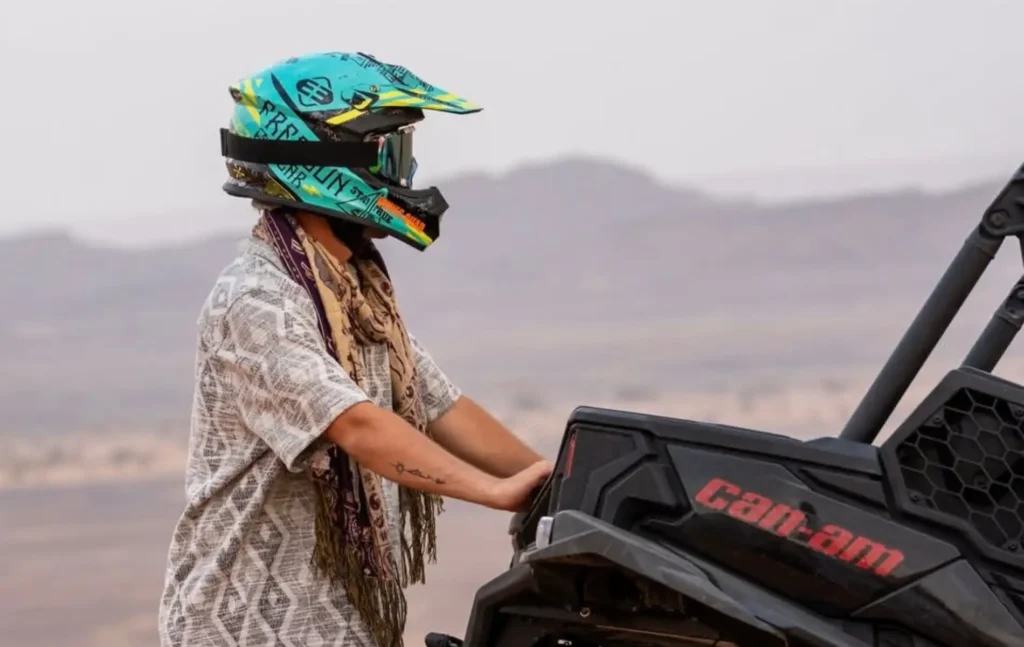 A traveler wearing a protective helmet and desert scarf standing next to a Can-Am buggy Merzouga desert tour.