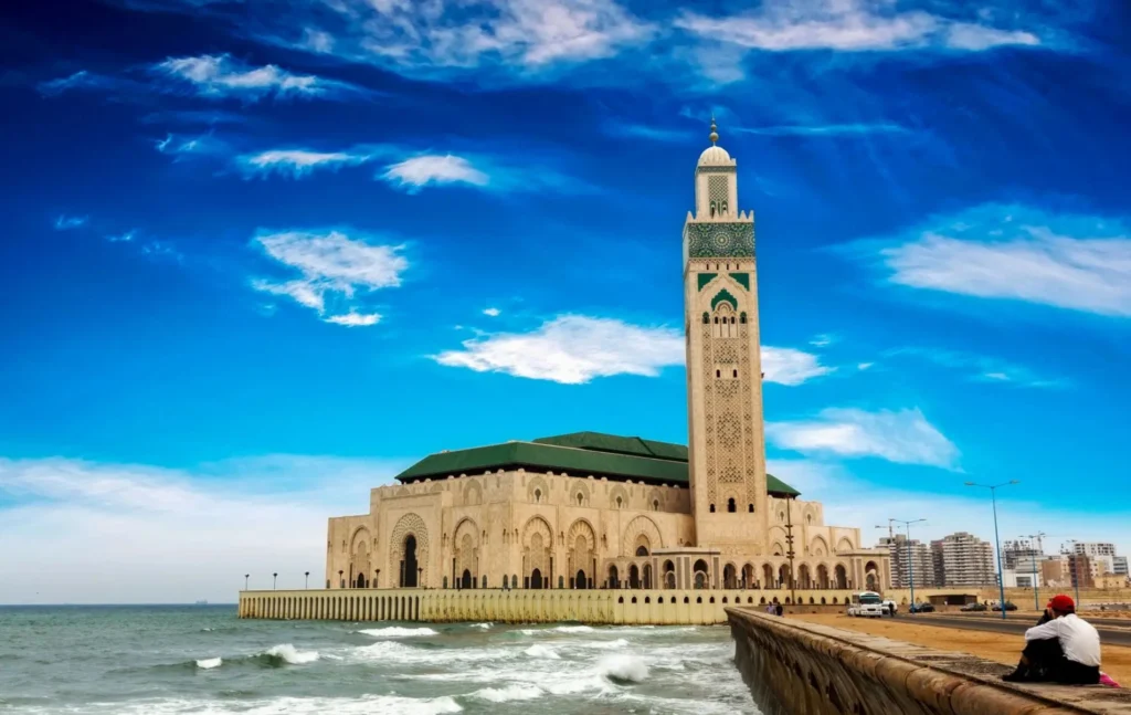 The grand Hassan II Mosque in Casablanca, Morocco, featuring its 210-meter minaret and intricate Moorish architecture against a clear blue sky—a highlight of a Morocco itinerary 8 days.