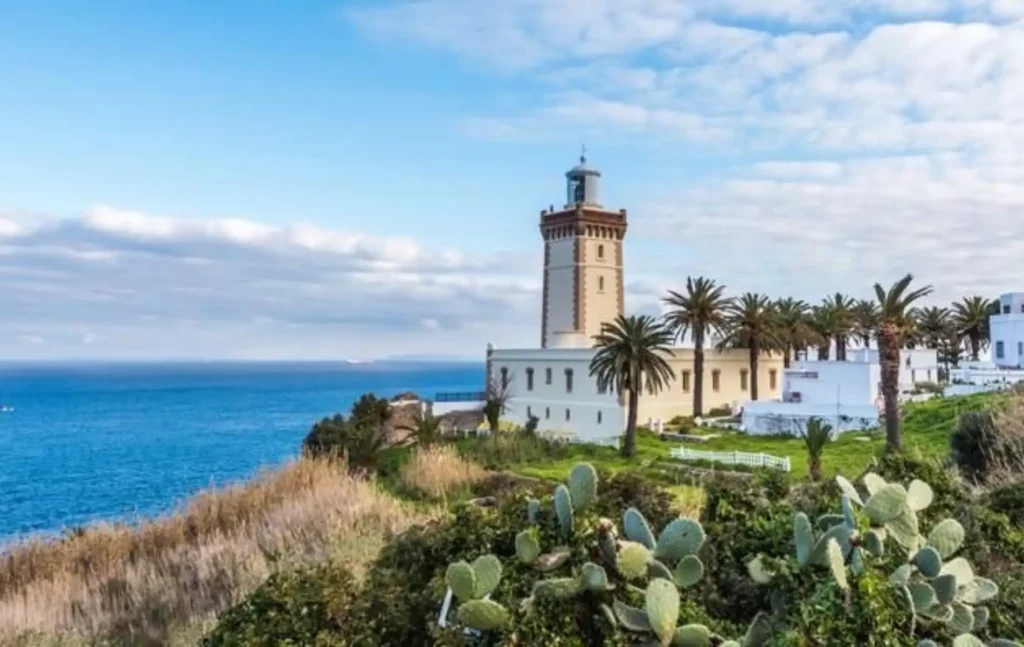 Morocco itineraries featuring the historic Cap Spartel lighthouse overlooking the Atlantic Ocean with palm trees and greenery in the foreground.