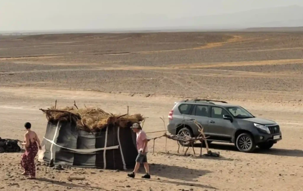 A 4x4 vehicle parked next to a traditional nomad tent during a 4 days tour from Marrakech to Merzouga, showing travelers visiting a local family in the desert.