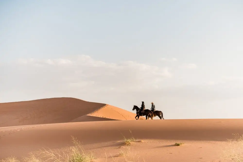 A pair of riders enjoying a Merzouga horse riding excursion across the vast, rolling landscape.