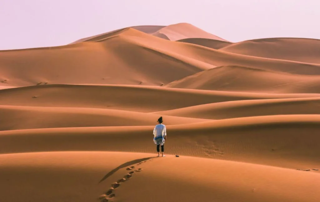 A lone traveler standing on a sand ridge with footprints leading behind them in the vast Erg Chebbi desert during a 5 day desert tour from marrakech.