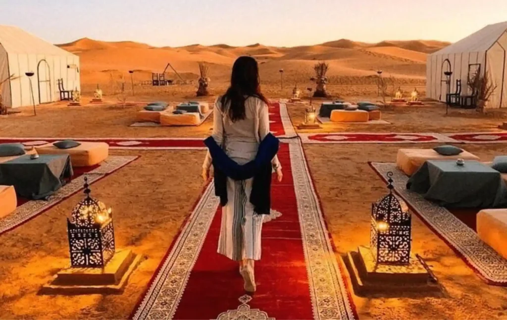 A woman walking on a red carpet through a luxury desert camp at sunset during a marrakech to fes desert tour 2 days.