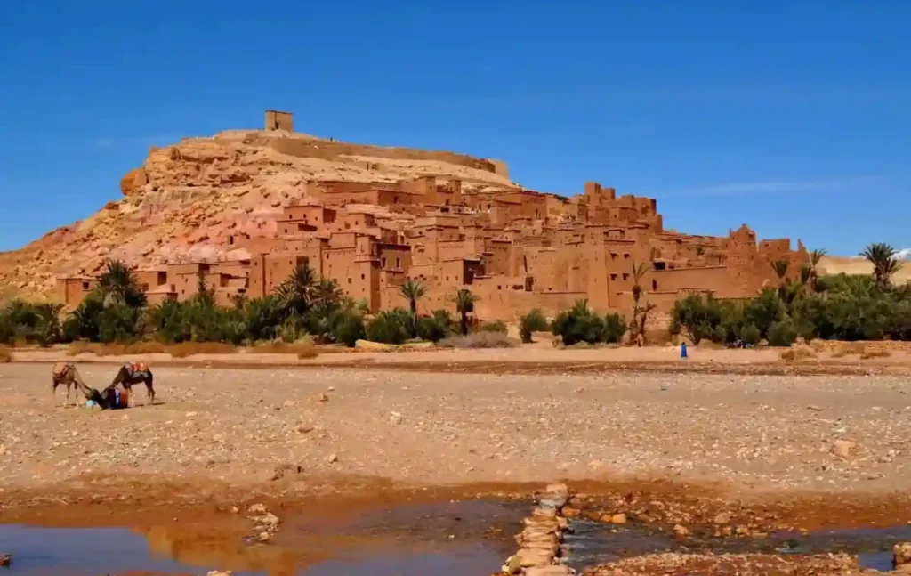 The historic earthen clay city of Ait Ben Haddou seen during a 2 day desert tour from marrakech with camels in the foreground.