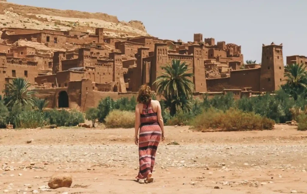 A traveler walking toward the historic mud-brick towers of Ait Ben Haddou on a fes to marrakech desert tour 2 days.