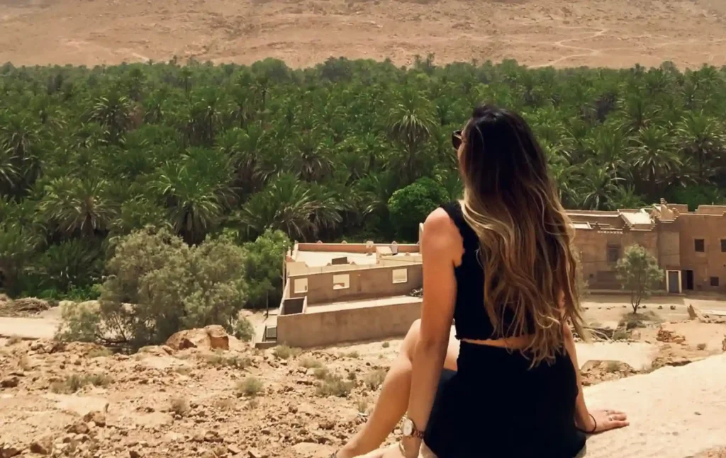 A traveler sitting on a ridge looking out over a lush green palm oasis during a fes to marrakech desert tour 2 days.