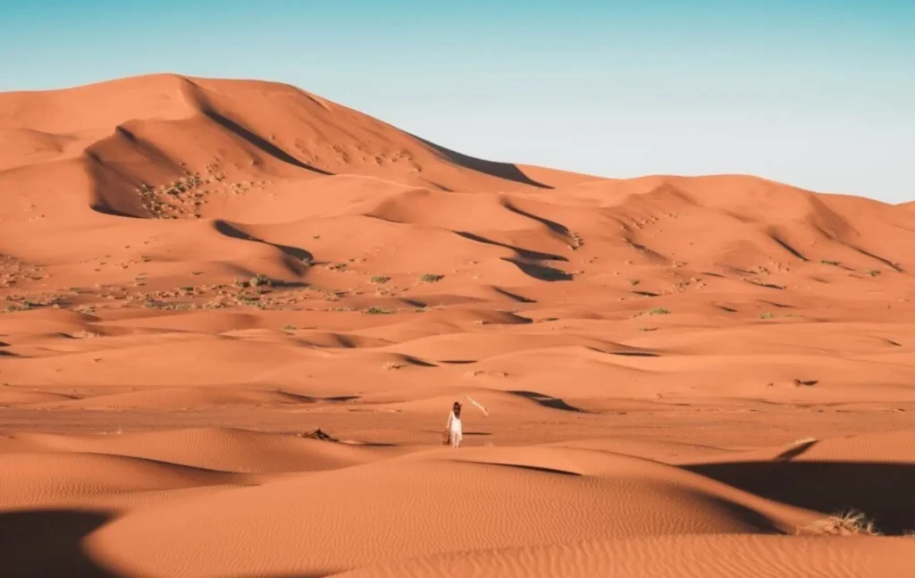 A traveler in a white dress walking through the vast, golden sand dunes of the Sahara Desert during a 4 days tour from Fes to Marrakech.