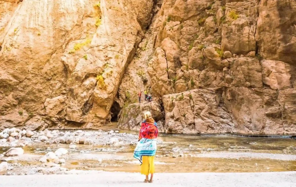 A traveler standing by the river beneath the towering rock walls of Todra Gorge during a 3 days desert tour from Fes to Marrakech.