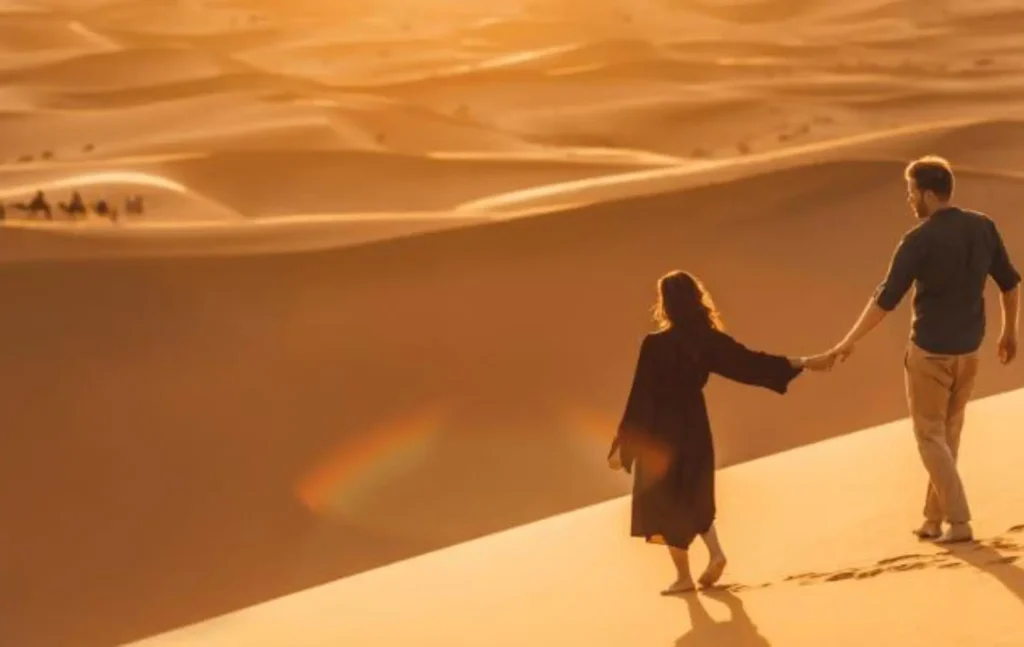 A couple holding hands and walking on top of a sand dune at sunset during a 2 days desert tour from fes.