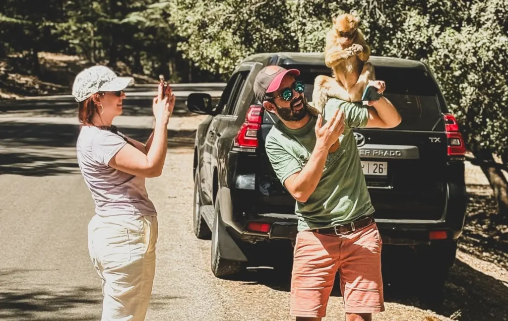 A traveler smiling with a Barbary macaque monkey on his shoulder during a 6 days tour from marrakech through the cedar forests.