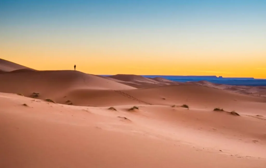 A lone traveler standing on top of a sand dune at sunset during a 2 days desert tour from marrakech to zagora.