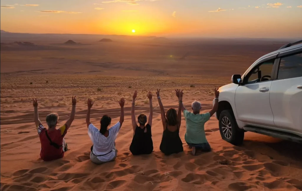 7 days morocco tour: travelers watching the sunrise over the sand dunes and mountains in Tafraout Sidi Ali with a white 4x4.