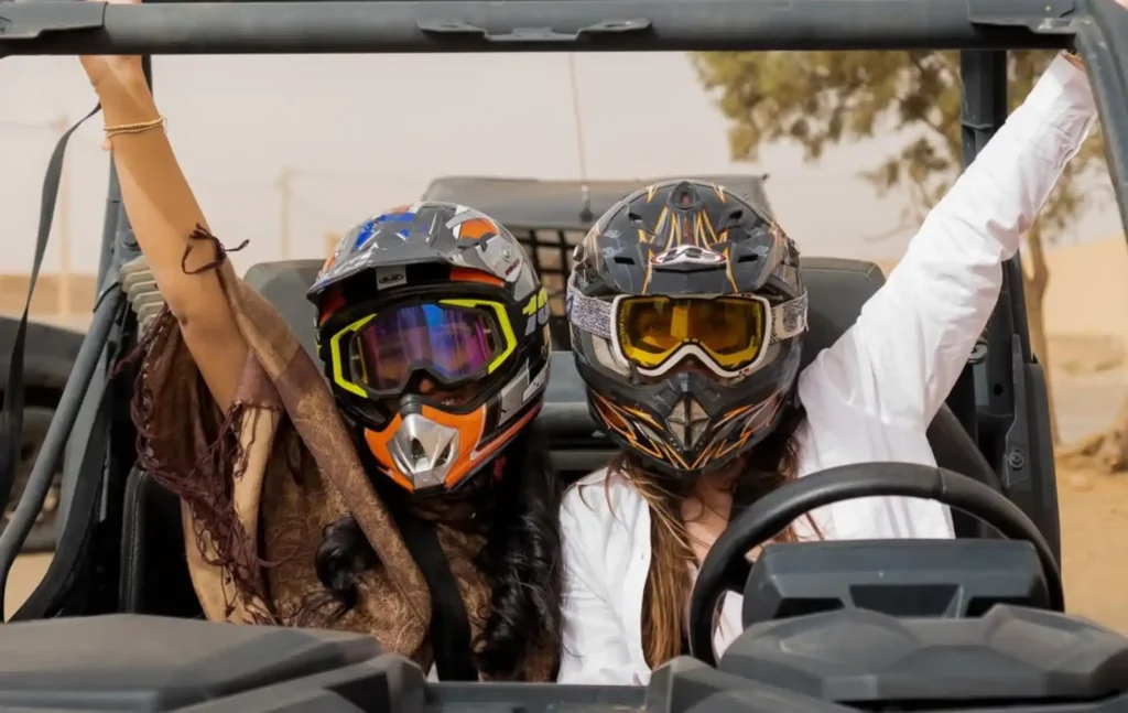 4 days morocco student trip: Two female students wearing professional off-road helmets and goggles cheering from inside a desert buggy during an excursion.