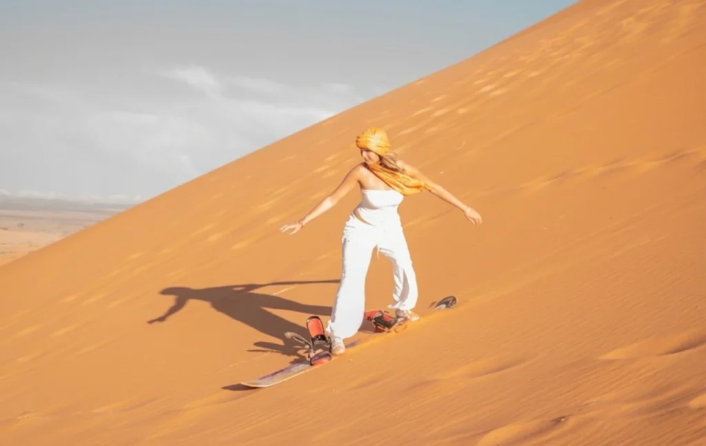 A woman sandboarding down a golden dune during a 5 days Morocco student trip.