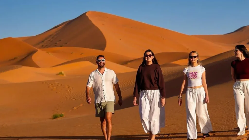A group of happy friends walking down golden sand dunes during Casablanca desert tours, an essential stop for any morocco itinerary.