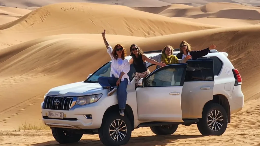 A group of female travelers posing excitedly on a white 4x4 Toyota Prado during Casablanca desert tours, a thrilling addition to their morocco itinerary.