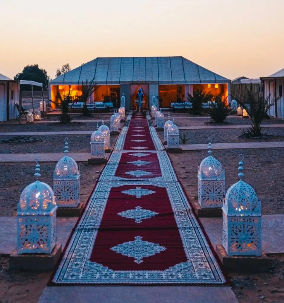 1 night in Merzouga desert experience walking down a red carpet lined with lanterns at a Merzouga luxury desert camp at twilight