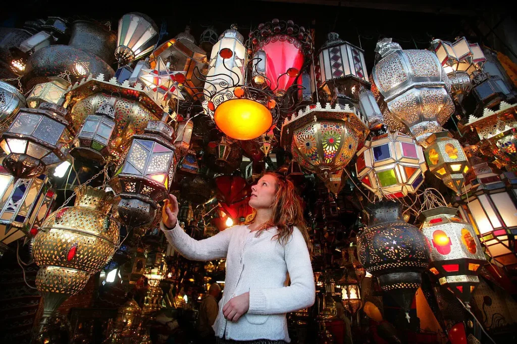 Is it Safe to Travel to Marrakech: A female tourist safely exploring a vibrant Moroccan lantern shop in a traditional souk market.