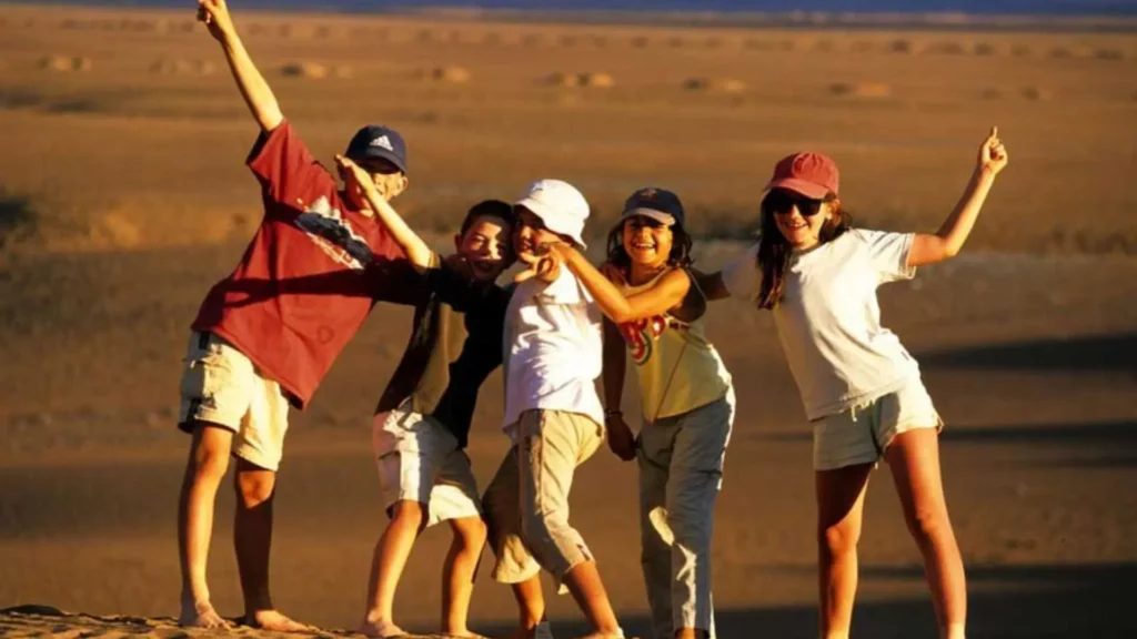 A group of happy kids smiling and having fun together outdoors in the desert during an exciting vacation with Morocco Family Tours.