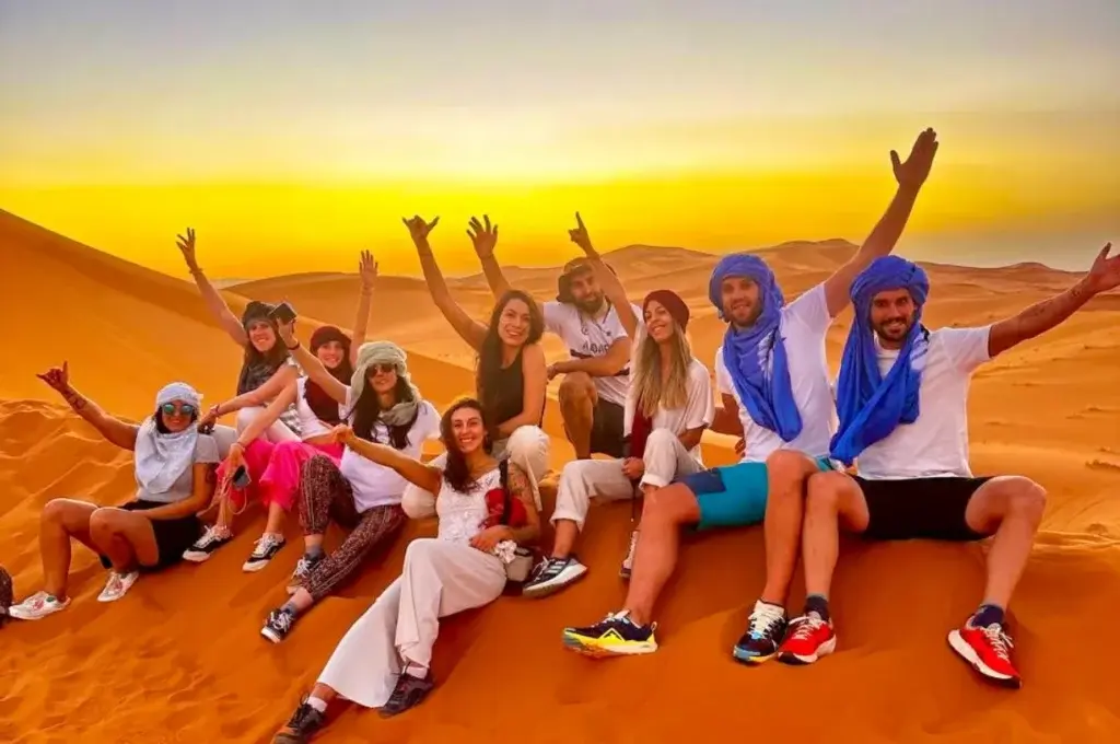 Group of travelers celebrating sunset on the Sahara dunes
