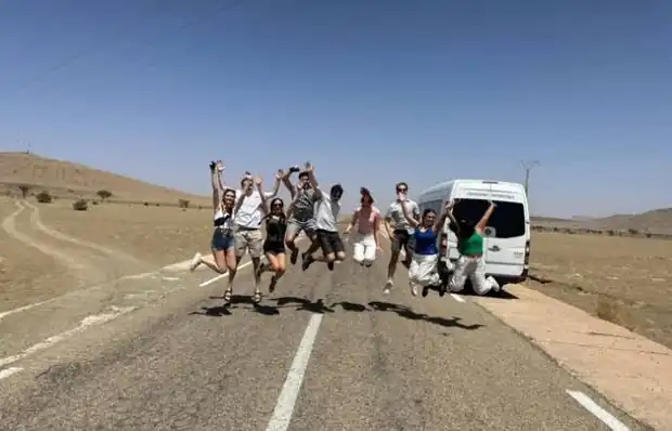 Students tours to Morocco: students jumping on a desert road next to our air-conditioned tour van