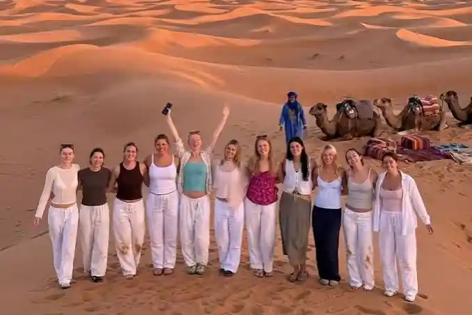 Students tours to Morocco: student group smiling on the Erg Chebbi dunes at sunset with camels behind