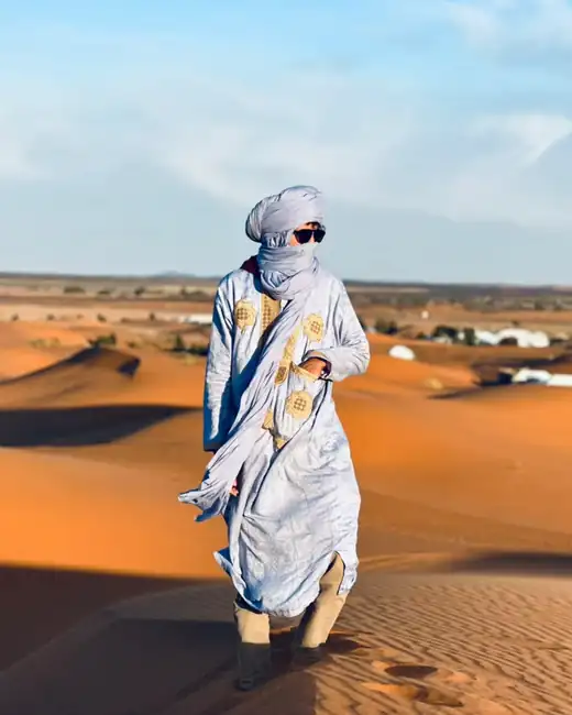 Berber guide in a traditional blue robe and turban walking on the Merzouga dunes